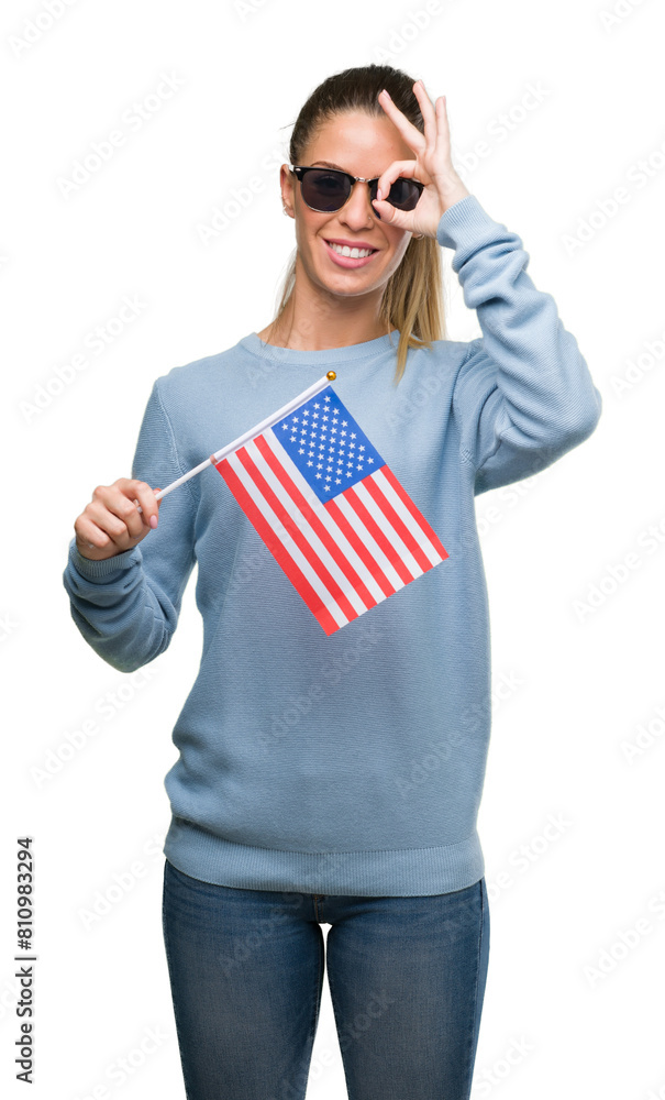 Wall mural Beautiful young woman holding USA flag with happy face smiling doing ok sign with hand on eye looking through fingers