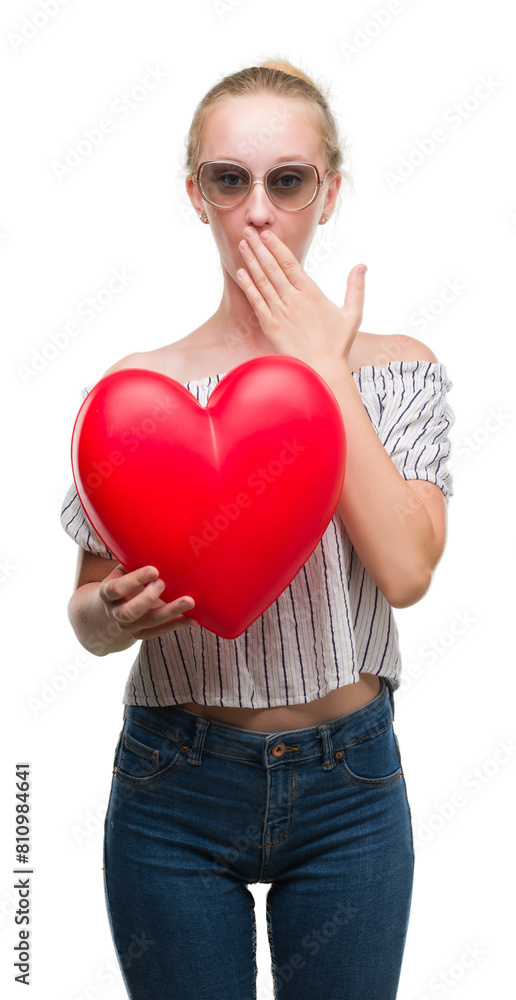 Canvas Prints Blonde teenager woman holding red heart cover mouth with hand shocked with shame for mistake, expression of fear, scared in silence, secret concept