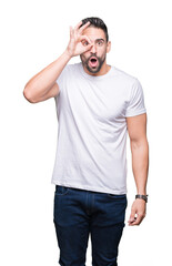 Fototapeta premium Young man wearing casual white t-shirt over isolated background doing ok gesture shocked with surprised face, eye looking through fingers. Unbelieving expression.