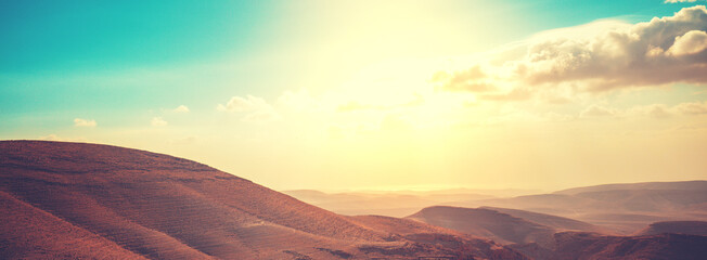 Mountainous desert with colorful cloudy sky. Judean desert in Israel at sunset. Horizontal banner - obrazy, fototapety, plakaty