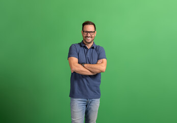 Portrait of handsome confident entrepreneur with arms crossed smiling and posing on green background
