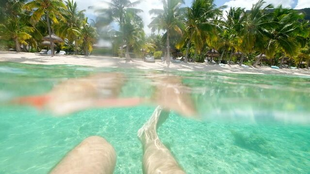 POV video of a man swimming in crystall clean waters of Le Morne lagoon waves at sandy beach with exotic luxury resort sun beds, umbrellas. Tropical vacations and traveling concept 4K footage.