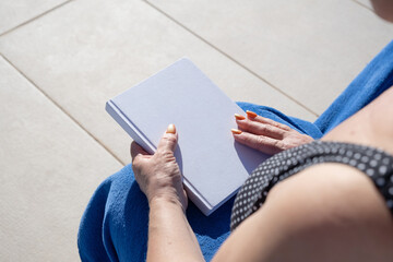 unrecognizable woman holding blank book for mockup design, sitting by the swimming pool