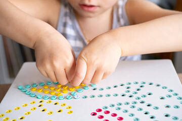 girl plays with mosaic, small parts in hands of child, fill in holes, fine motor skills...