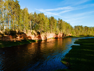 panoramic view of the red cliffs along the riverbank in latvia with lush forest and vibrant water