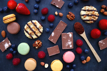 Macarons, chocolate, cookies, berries and various nuts on dark blue background. Top view.