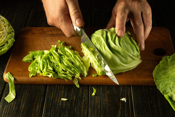 The chef cuts young fresh cabbage with a knife to prepare a salad. Low key concept of preparing a...