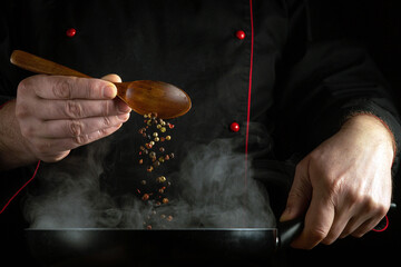 Spoon dry pepper into a hot pan for flavor. Close-up of a chef hands preparing aromatic food.