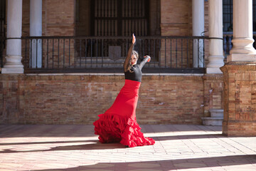 Young, beautiful, brunette woman in black shirt and red skirt, dancing flamenco between marble columns in Spain square in Seville. Flamenco concept, dance, art, typical Spanish.