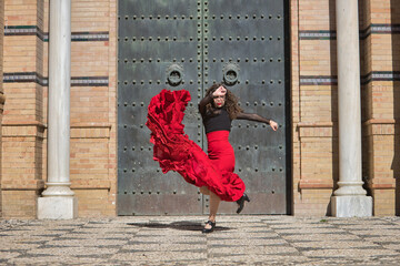 Young, beautiful, brunette woman in black shirt and red skirt, dancing flamenco in front of an old,...