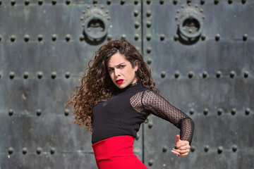 Portrait of young, beautiful, brunette woman in black shirt and red skirt, dancing flamenco with old, black metal door in the background. Flamenco concept, dance, art, typical Spanish.