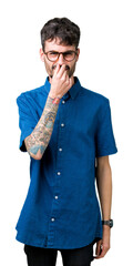 Young handsome man wearing glasses over isolated background smelling something stinky and...