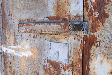 A very old rusty metal door with a lock with peeling paint. 