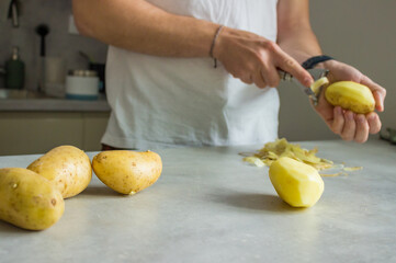 a man peeling potatoes on a grey kitchen counter with a potato peeler
