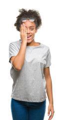 Young afro american woman wearing glasses over isolated background covering one eye with hand with confident smile on face and surprise emotion.