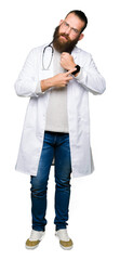 Young blond doctor man with beard wearing medical coat In hurry pointing to watch time, impatience, upset and angry for deadline delay