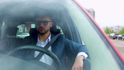 Young businessman sitting in the car and using seat belt while driving to work in the city....