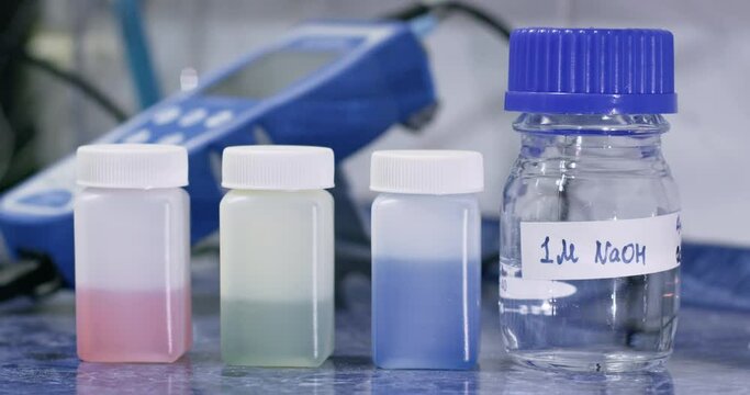Lab worker adjusts bottle with sodium hydroxide solution near color fluids on table closeup. Chemical reagents for experiment conducting