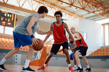 Multiracial group of men playing basketball at indoor court.