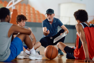 Mature coach explaining game tactics to basketball players during sports training.