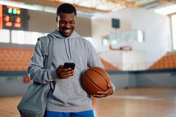 Happy black athlete texting on cell phone after basketball practice.