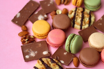 Pastel macarons, almond chocolate, peanut butter cookies and various nuts on bright pink background. Selective focus.