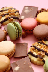 Pastel macarons, almond chocolate, peanut butter cookies and various nuts on bright pink background. Selective focus.