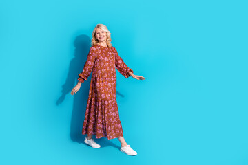 Fototapeta premium Full length photo of shiny attractive lady dressed brown clothes smiling walking empty space isolated blue color background