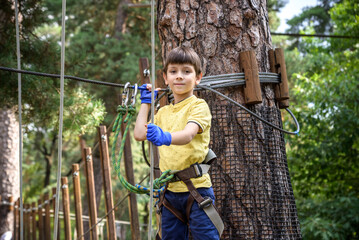 Strong excited young boy playing outdoors in rope park. Caucasian child dressed in casual clothes and sneakers at warm sunny day. Active leisure time with children concept