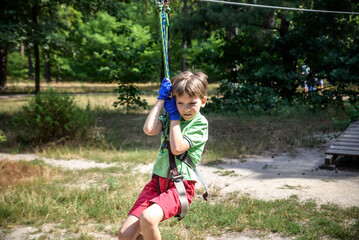 Strong excited young boy playing outdoors in rope park. Caucasian child dressed in casual clothes and sneakers at warm sunny day. Active leisure time with children concept