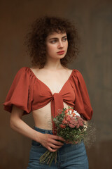 A beautiful curly-haired girl in a brown blouse and jeans holding a bouquet of spring flowers and...