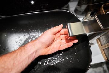 A man's hand touches the water and washes his hands with soap. A black sink with a silver faucet...