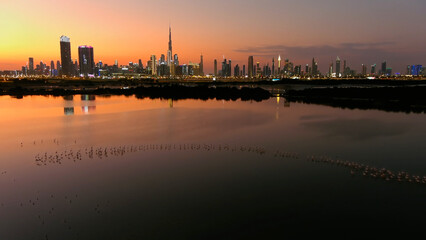 Dubai Skyline at sunset with Lake and flamingo drone view 
Drone view from Dubai at sunset, lake and flamingo flock, 2022
