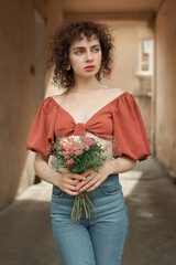 Curly-haired girl in brown blouse and jeans holding a bouquet of spring flowers. Grain effect used