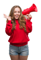 Young blonde woman holding red megaphone very happy and excited, winner expression celebrating victory screaming with big smile and raised hands