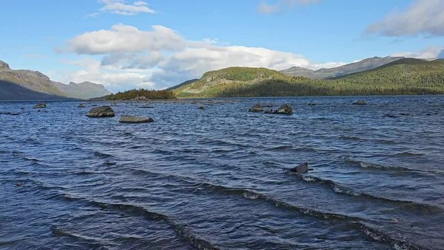 Strong wind whips the water surface of Lake Langas in Saltoluokta, Sweden, in the morning light and blue sky with clouds, on the Kungsleden long-distance hiking trail
