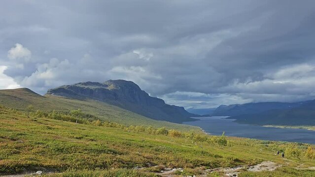Dramatic light after a storm with a rainbow on the horizon - over Lake Langas in the Saltoluokta Valley, with the golden hues of Swedish Lapland and yellow birch leaves swaying in the wind