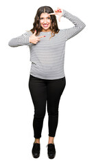 Young beautiful woman wearing stripes sweater smiling making frame with hands and fingers with happy face. Creativity and photography concept.