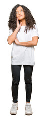 Fototapeta premium Young beautiful woman with curly hair wearing white t-shirt with hand on chin thinking about question, pensive expression. Smiling with thoughtful face. Doubt concept.