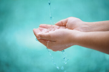 Person, hands and water with drops for natural hydration, hygiene or sustainability on a blue...