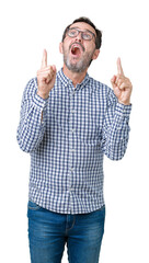 Handsome middle age elegant senior business man wearing glasses over isolated background amazed and surprised looking up and pointing with fingers and raised arms.