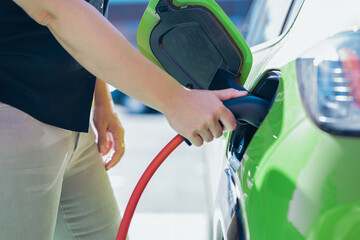 anonymous person is charging electric car or ev in the station. The woman uses the power cord and...