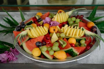 A round plate full of exotic fruits, pineapple, grapes, strawberries, apricots, peaches, watermelons, kiwis and more