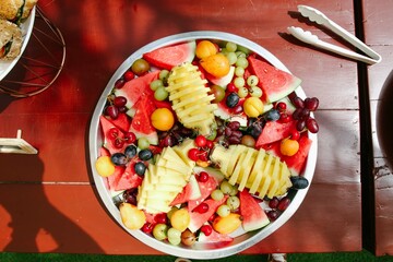 A round plate full of exotic fruits, pineapple, grapes, strawberries, apricots, peaches, watermelons, kiwis and more