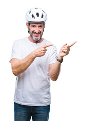 Middle age senior hoary cyclist man wearing bike safety helment isolated background smiling and looking at the camera pointing with two hands and fingers to the side.