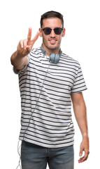 Handsome young man wearing headphones smiling looking to the camera showing fingers doing victory sign. Number two.