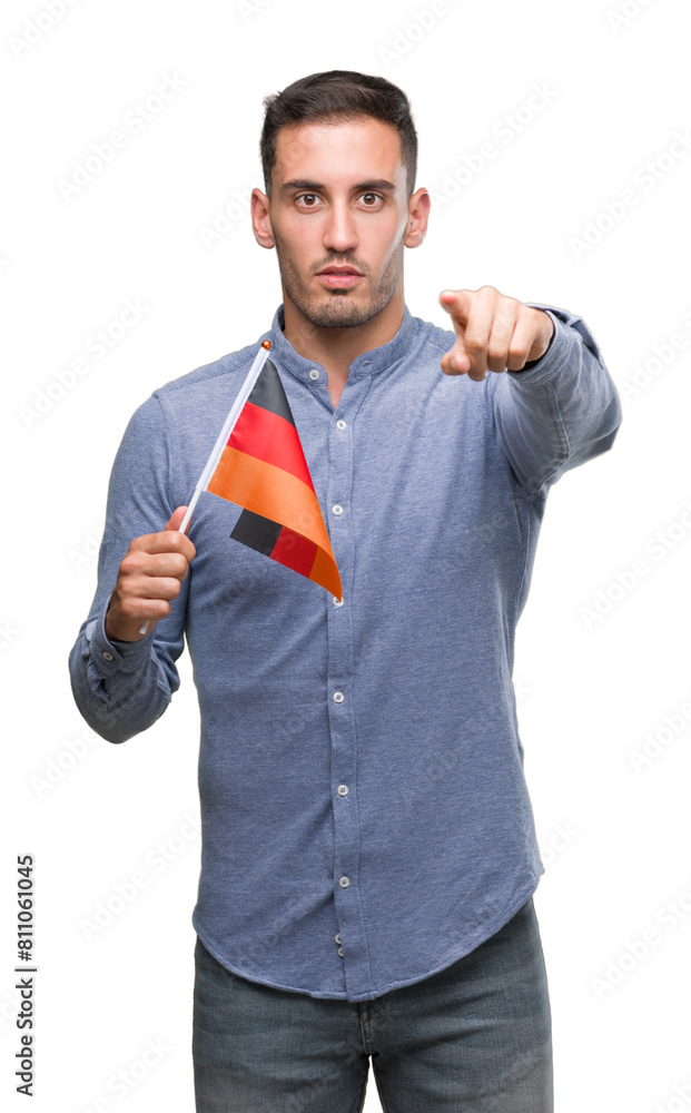 Wall mural Handsome young man holding a flag of Germany pointing with finger to the camera and to you, hand sign, positive and confident gesture from the front