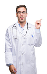 Handsome young doctor man with a big smile on face, pointing with hand and finger to the side looking at the camera.