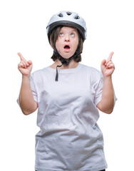 Young adult cyclist woman with down syndrome wearing safety helmet over isolated background amazed and surprised looking up and pointing with fingers and raised arms.
