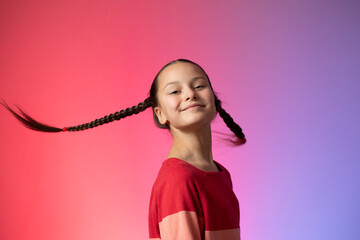 Portrait of preteen smiling girl turning her head with flying pigtails against pink background
